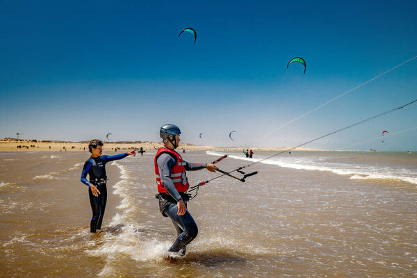 Essaouira, Morocco - August 3, 2023: A kitesurf instructor teaches a man to maneuver the kite on the beach. The place is renowned for kitesurfing lovers, thanks to the strong wind, always present, which allows you to easily lift the kite in flight.