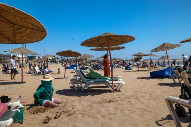 Essaouira, Fas - 3 Ağustos 2023: Plajdaki kadın tamamen tipik kıyafet ve şapkayla kaplı. Şehir hayatı