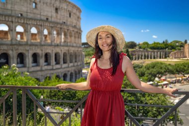 Hasır şapkalı esmer kız Kolezyum 'un ihtişamına hayran ve arka planda İtalya, Roma Forumu' nun antik kalıntıları..