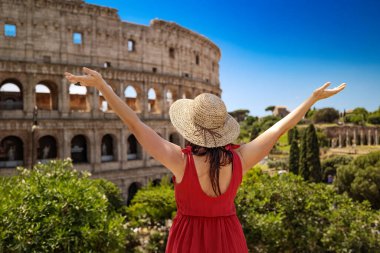 Hasır şapkalı, Roma 'yı ziyaret eden mutlu kız seviniyor ve kollarını kaldırıyor. Kolezyumun ihtişamı ve arka plandaki Roma Forumu' nun antik harabeleri önünde..