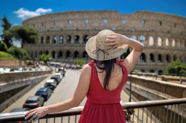 Hasır şapkalı ve kırmızı elbiseli esmer kız İtalya 'daki antik Kolezyum' a hayran. Turist antik Roma 'nın en ünlü anıtını ziyaret eder..