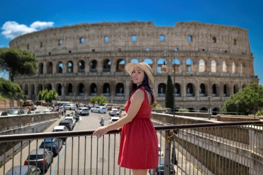 Hasır şapkalı ve kırmızı elbiseli esmer kız İtalya 'daki antik Kolezyum' a hayran. Turist antik Roma 'nın en ünlü anıtını ziyaret eder..