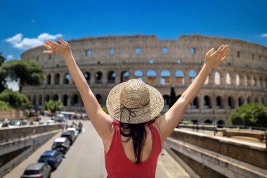 Hasır şapkalı bir kız İtalya 'da Roma' ya turist ziyaretinde, kollarını kaldırarak antik Kolezyum 'un ihtişamının önünde seviniyor ve kollarını kaldırıyor..