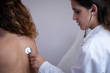 Doktor, hastanın göğsünü steteskopla dinler. Organizmanın nefes alışını ve iç seslerini gözlemler. Geleneksel tıbbi muayene.