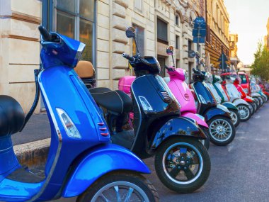 Bir dizi renkli scooter cadde boyunca bir sıra halinde park edilmiş, şehirde scooter kiralama yeri var..