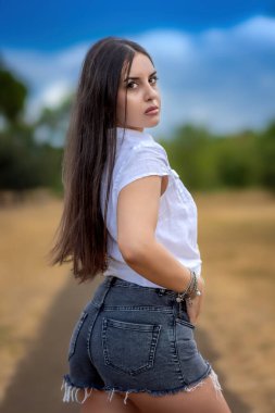 Doğa parkında uzun saçlı, kot pantolonlu ve bluzlu esmer bir kızın portresi..