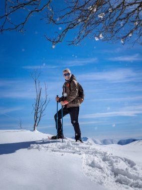 Kar ayakkabılarıyla karda yürüyen aktif sportif bir adam, arka planda kış dağlarının karlı dağlarında.