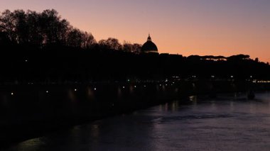 Roma, İtalya - 31 Mart 2025: Tiber Nehri üzerindeki şehirde gün batımı ve arka planda Vatikan 'daki Aziz Peter Bazilikası kubbesi.