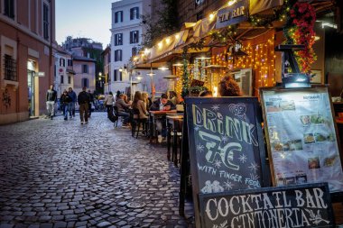 Roma, İtalya - 31 Mart 2025: Trastevere 'de, açık tablolarda ve menülerde sergilenen turistlerin sıkça uğraştığı tipik bir kafe restoranı. Lokantaların rahatı için aydınlatma ve gaz ısıtıcıları.