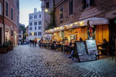 Roma, İtalya - 31 Mart 2025: Trastevere 'de, açık tablolarda ve menülerde sergilenen turistlerin sıkça uğraştığı tipik bir kafe restoranı. Lokantaların rahatı için aydınlatma ve gaz ısıtıcıları.