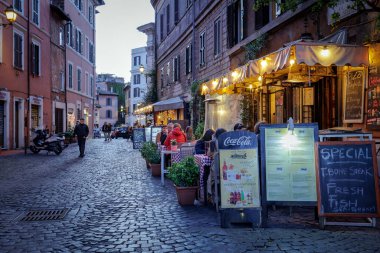 Roma, İtalya - 31 Mart 2025: Trastevere 'de, açık tablolarda ve menülerde sergilenen turistlerin sıkça uğraştığı tipik bir kafe restoranı. Lokantaların rahatı için aydınlatma ve gaz ısıtıcıları.