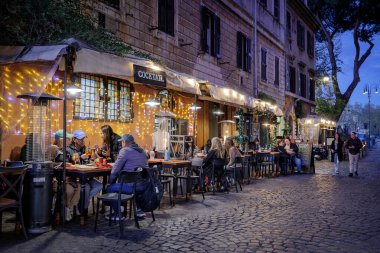 Roma, İtalya - 31 Mart 2025: Trastevere 'de, açık tablolarda ve menülerde sergilenen turistlerin sıkça uğraştığı tipik bir kafe restoranı. Lokantaların rahatı için aydınlatma ve gaz ısıtıcıları.