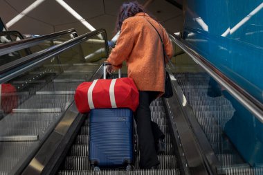 Napoli, İtalya - 18 Nisan 2025: Elinde bavul ve kırmızı spor çantasıyla gezen bir kadın, şehirdeki bir metro istasyonunda yürüyen merdivenden yukarı çıkıyor..