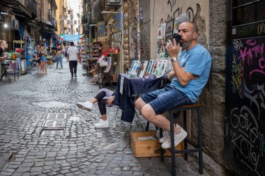 Napoli, İtalya - 19 Haziran 2025 Via San Biagio dei Librai 'deki tarihi şehir merkezinde bir adam ve hediye tezgahı.