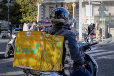Napoli, İtalya - 18 Nisan 2025: Glovo kuryesi sırtında bir sırt çantası ve scooter ile şehre doğru yola çıktı. Vatandaşlara yaşam tarzı ve hizmetler.
