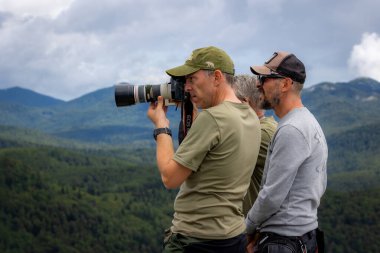 Koritnice, Slovenya - 27 Temmuz 2025: Bir vahşi yaşam fotoğrafçısı telefoto lensini dağda göstererek yırtıcı kuşların uçarken fotoğraflarını çekmeye çalışıyor. Koritnice, Slovenya
