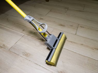 Ahşap zeminde sarı ve gri bir paspas..