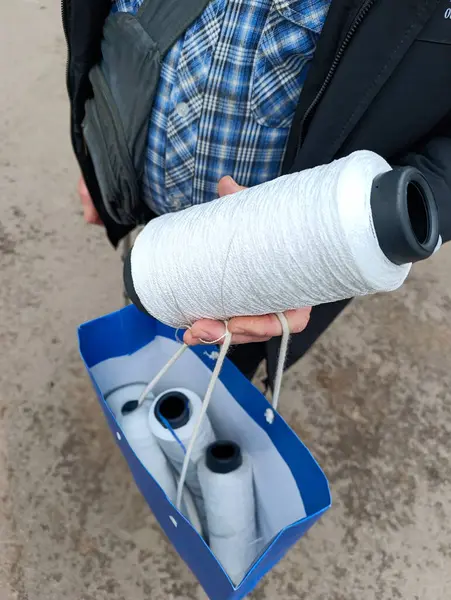 İçinde üç makara iplik olan mavi bir kutu tutan bir adam..