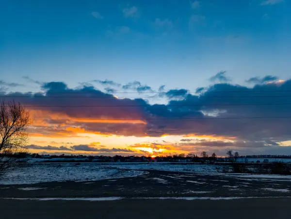 Önünde elektrik hatları olan karlı bir tarlanın üzerinde gün batımı..