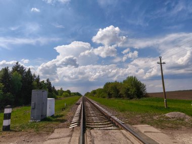 Bulutlu bir gökyüzünün altındaki çimenli bir arazinin ortasında bir tren yolu..