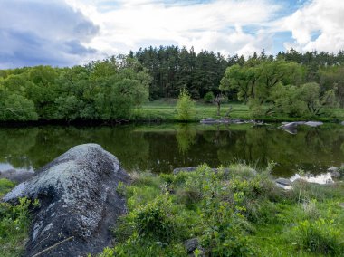 Ağaçlarla çevrili küçük bir göletin ortasında büyük bir kaya..
