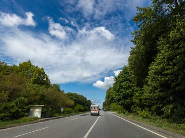 İki tarafında ağaçlar olan bir kamyonet yolda ilerliyor..