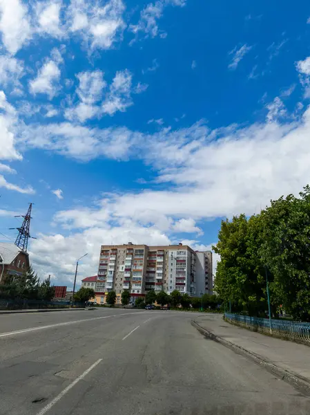 Mavi gökyüzünün altındaki yüksek bir binanın önündeki boş bir cadde..