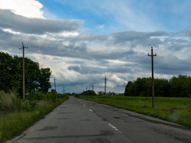 Bulutlu bir gökyüzünün altında çimenli bir tarlanın ortasında boş bir yol..