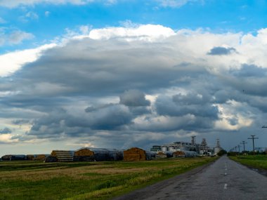 Bulutların altında bir otlağın ortasında boş bir yol ve arka planda tarımsal girişim..