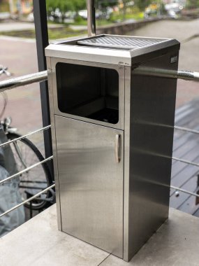 Paslanmaz çelik bir çöp tenekesi kaldırımda bisikletin yanında duruyor..