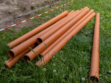 Bir grup turuncu boru, kırmızı ve beyaz şeritli bariyerin yanında çimlerin üzerinde yatıyordu..