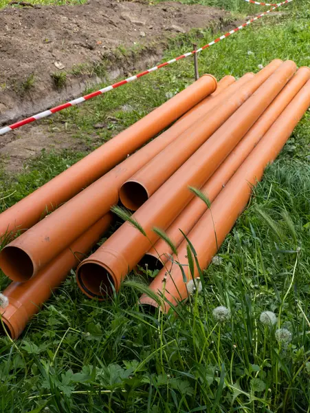 Bir grup turuncu boru çimlerin üzerinde yatıyor..