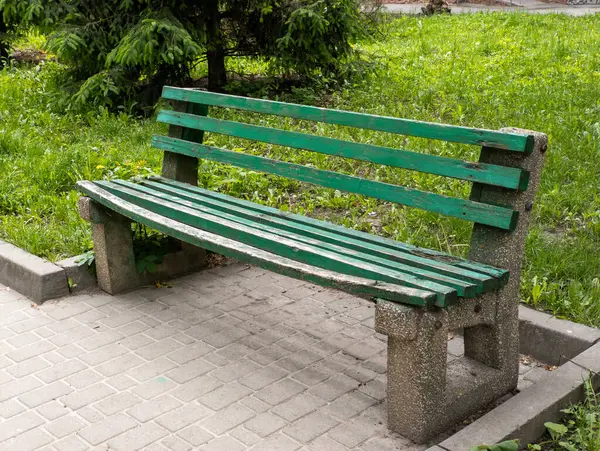 Parktaki kaldırım taşlarının üzerinde duran yeşil bank..