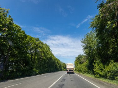 İki tarafında ağaçlar olan bir kamyonet yolda ilerliyor..