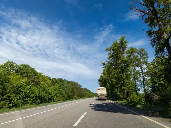 İki tarafında ağaçlar olan bir kamyonet yolda ilerliyor..