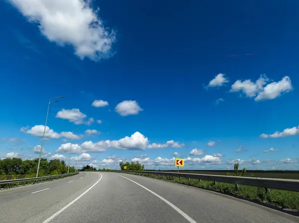 Arka planda bulutlar ve mavi gökyüzü olan uzun ve boş bir yol..