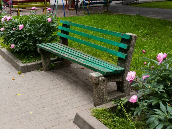 Çiçek bahçesinin ortasında duran yeşil bir park bankı..