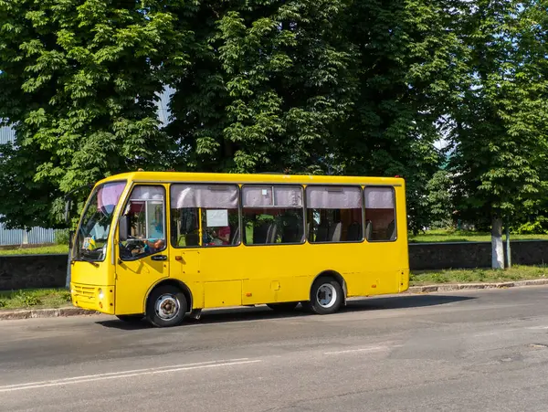 Ağaçların yanındaki caddeden geçen sarı bir otobüs..