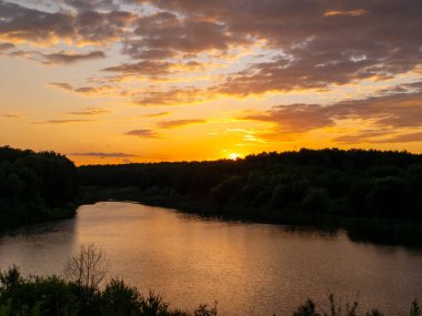 Arkasında ağaçlar olan bir su kütlesinin üzerinde gün batımı.