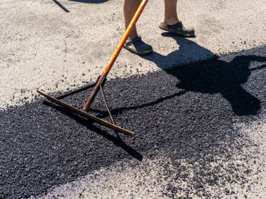 Bir adam bir otoparkın asfaltını temizlemek için tırmık kullanıyor..
