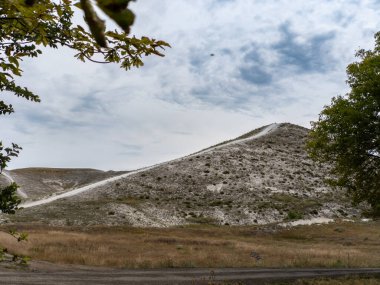 Bir tepenin yanındaki çim tarlasının ortasında toprak bir yol..
