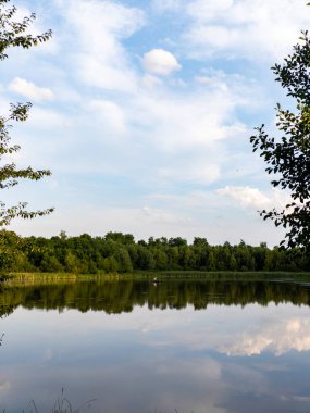 Ağaçlar ve bulutlarla çevrili bir su kütlesi..