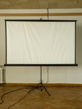 Tahta zemini olan bir odada tripodun üzerindeki projektör ekranı.