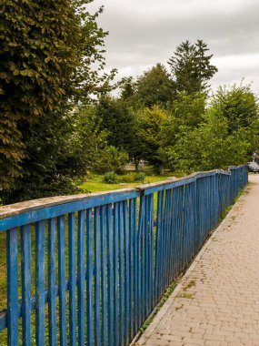 Çimenli bir alanın yanındaki kaldırımın kenarında mavi bir çit..