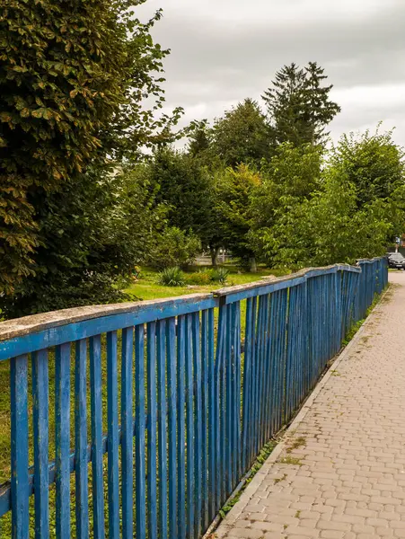 Çimenli bir alanın yanındaki kaldırımın kenarında mavi bir çit..