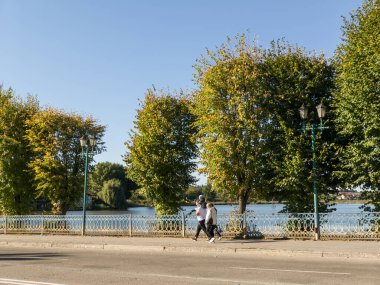 A couple of people walking down a street next to a body of water.