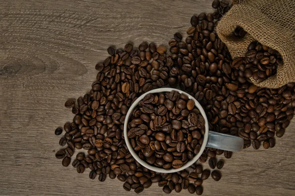 茶色のローストコーヒー豆のトップビューは 完全なコーヒーマグカップ イメージとテーブルの上にこぼれた ロイヤリティフリーのストック写真