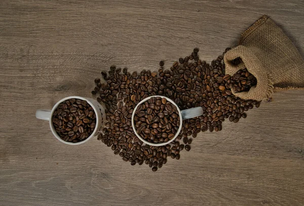 茶色のローストコーヒー豆のトップビューは 完全なコーヒーマグカップ イメージとテーブルの上にこぼれた ロイヤリティフリーのストック画像