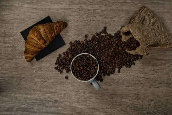 茶色のローストコーヒー豆のトップビューは 完全なコーヒーマグカップとビスケット イメージとテーブルの上にこぼれた ストック写真