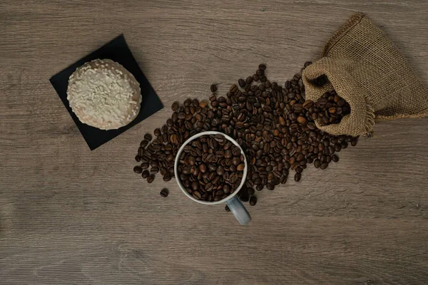 茶色のローストコーヒー豆のトップビューは 完全なコーヒーマグカップとビスケット イメージとテーブルの上にこぼれた ストック画像